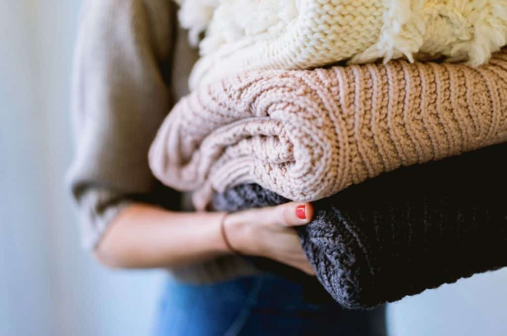 LADY HOLDING A PILE OF WOOLEN FOLDED LAUNDRY